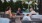A group of people at an outside circular table, talking with trees in the background