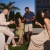 A group of people talking and holding drinks outside next to plants