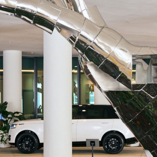 Touch Sculpture Welcomes You To Aster & Links Sculpture of Hand with Vehicle in Background